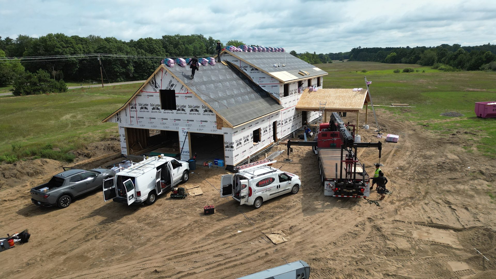 Northlight crew and trucks on a large new build, roof dried in and shingle bundles staged, seen from the air