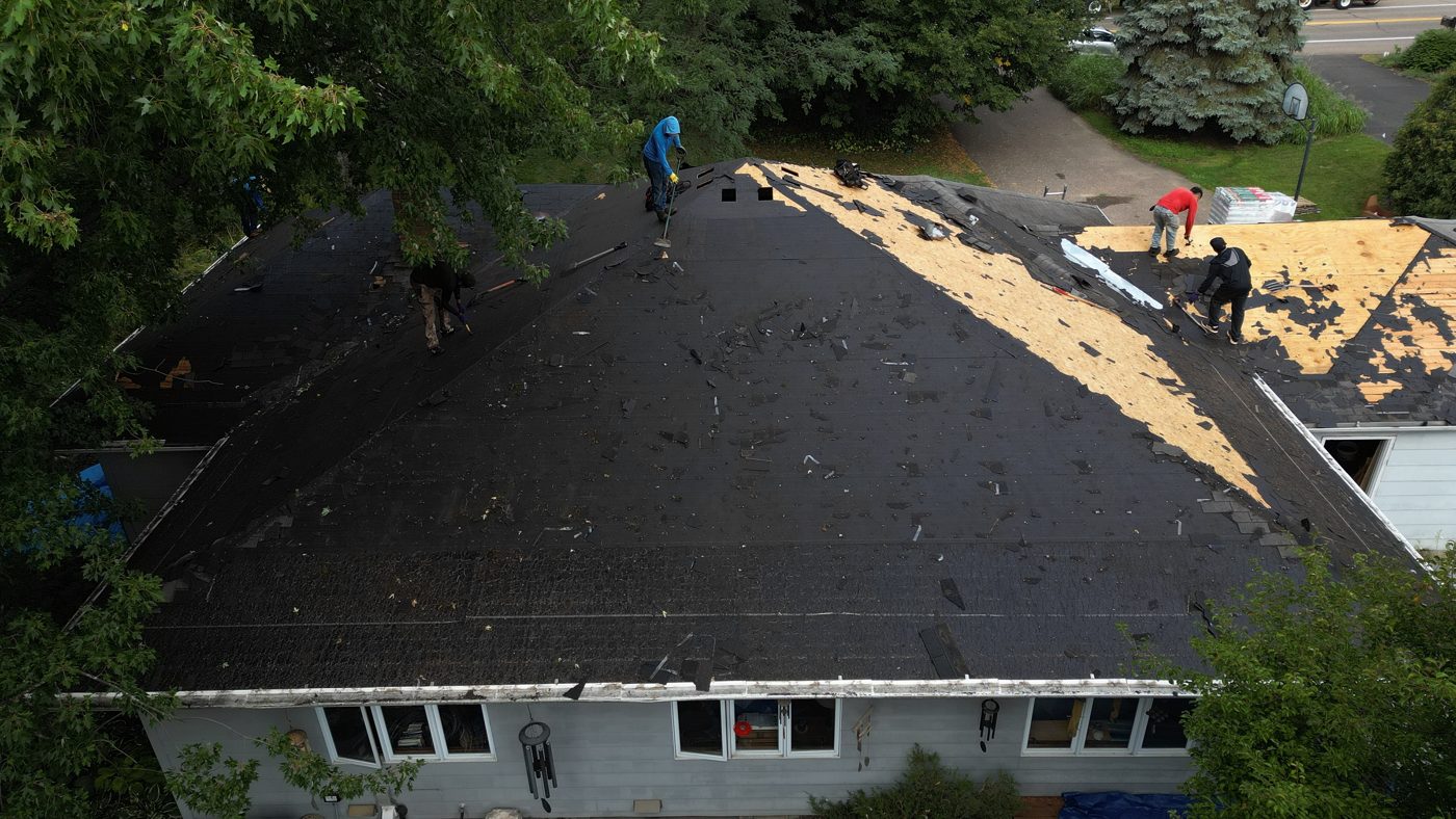 Crew tearing off an old roof down to the deck, seen from a drone